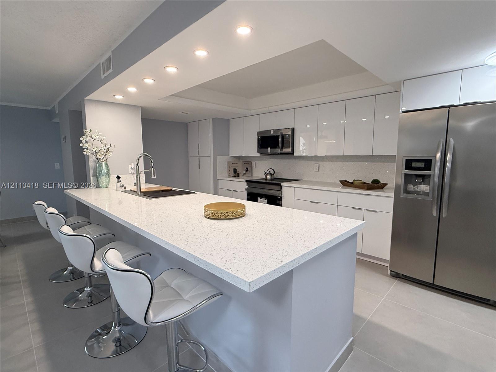 Kitchen featuring white high-gloss cabinetry, stone-finish countertops, stainless steel appliances, recessed ceiling lighting, and large-format tile flooring