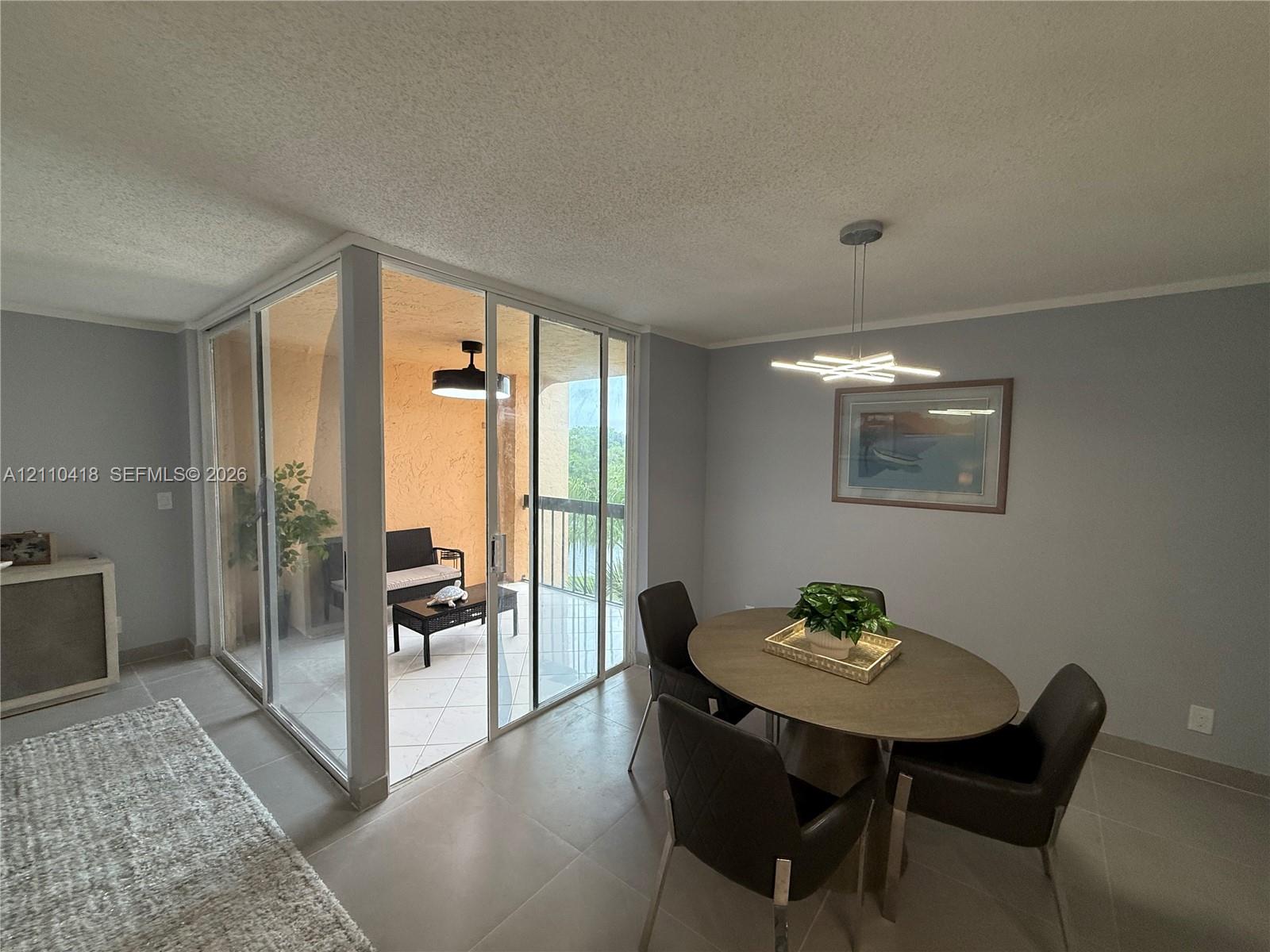 Enclosed balcony featuring floor-to-ceiling glass paneling and tile flooring, paired with large-format neutral floor tiling throughout and a contemporary geometric pendant light fixture