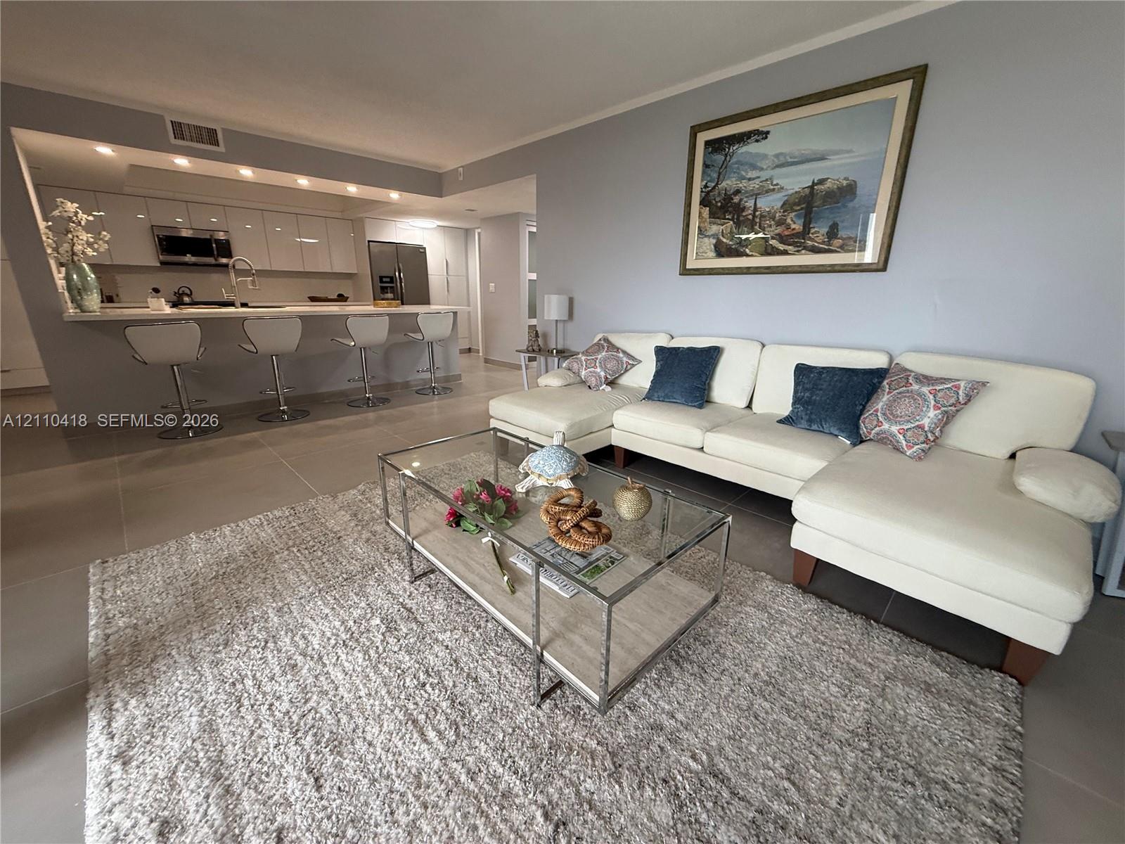 Open-concept kitchen featuring high-gloss cabinetry, stone countertops, and integrated recessed lighting, complemented by large-format tile flooring