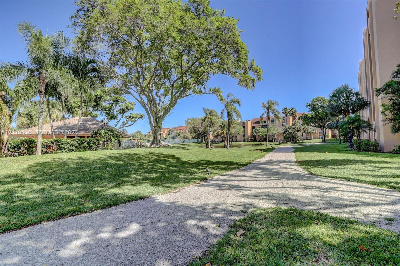 Landscaped grounds featuring mature canopy trees, palm trees, expansive grass lawns, and a paved stone pathway