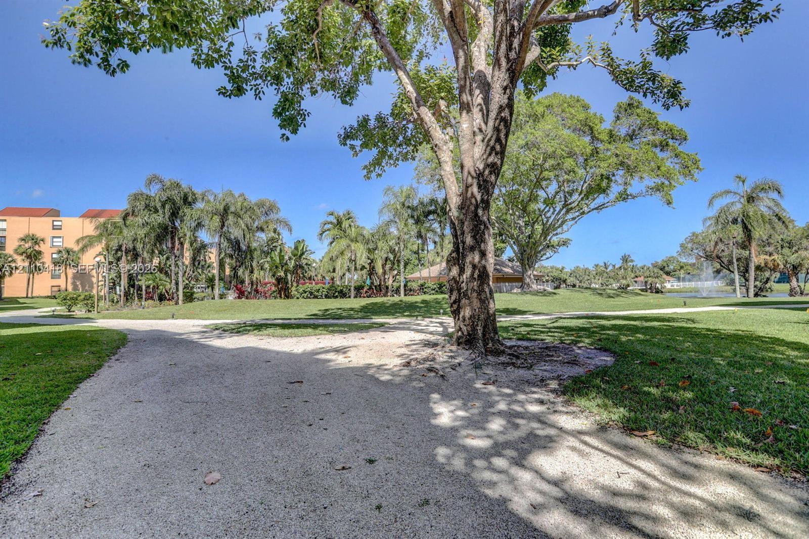 Expansive grounds featuring a meandering gravel pathway, mature trees, manicured lawns, and palm landscaping