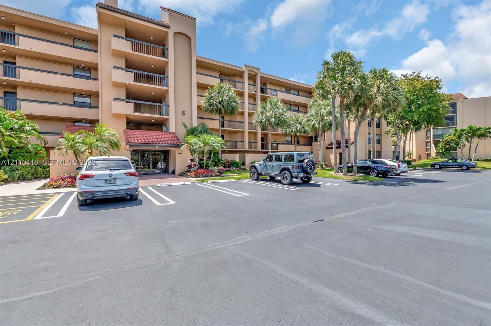 Multi-story residential building featuring covered balconies, terracotta-style roof accents, and mature palm tree landscaping