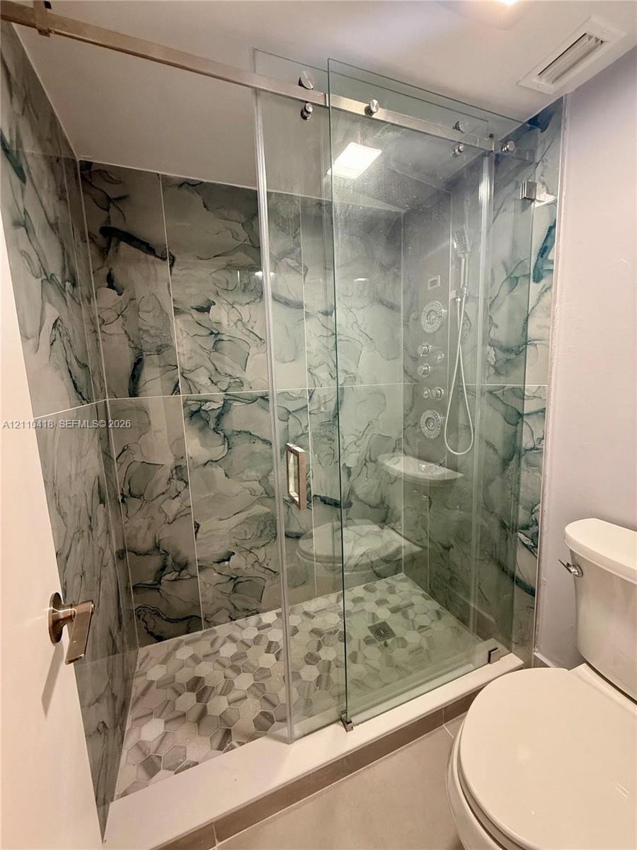 Walk-in shower featuring large-format patterned wall tile, hexagonal floor tiling, a frameless glass sliding door, and integrated body spray jets
