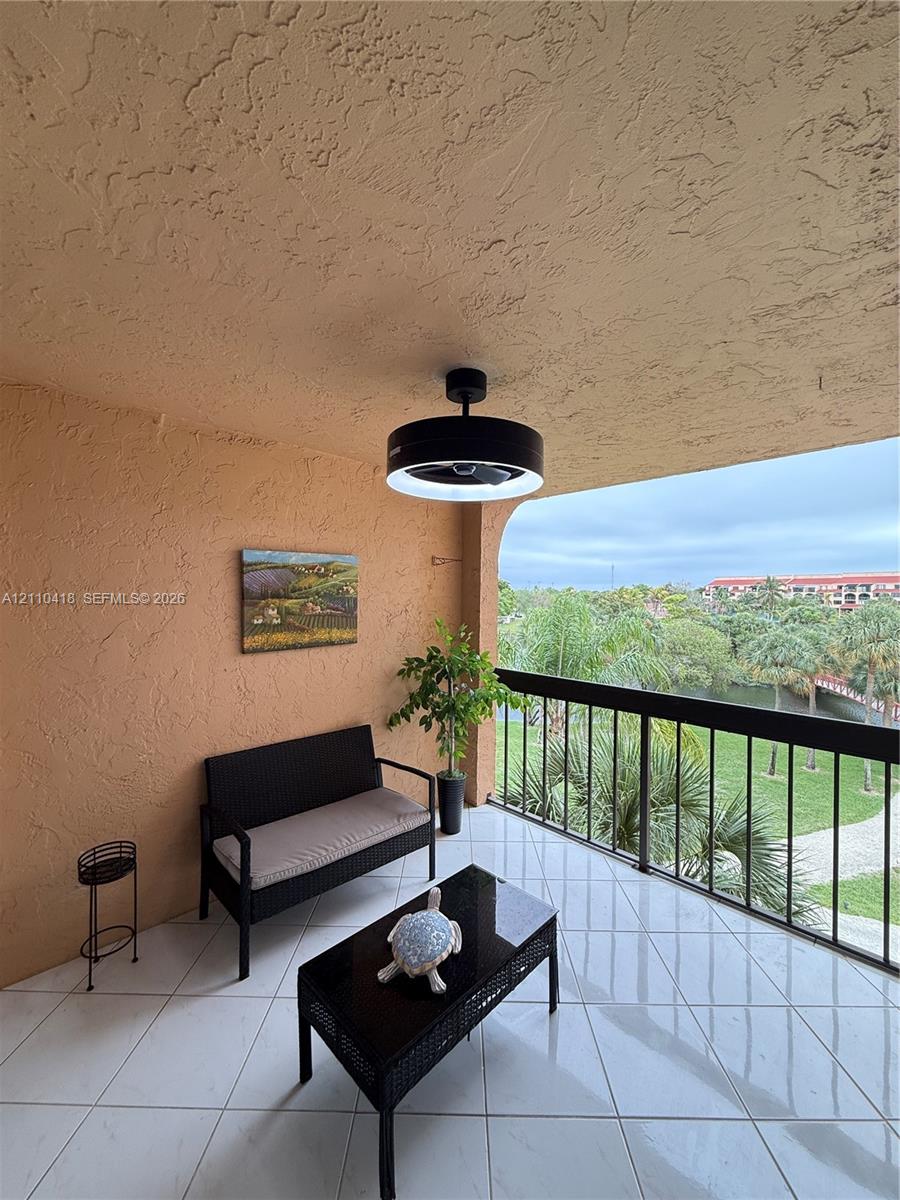 Covered balcony featuring white tile flooring, textured wall finishes, and a matte black ceiling fan with an integrated circular light fixture