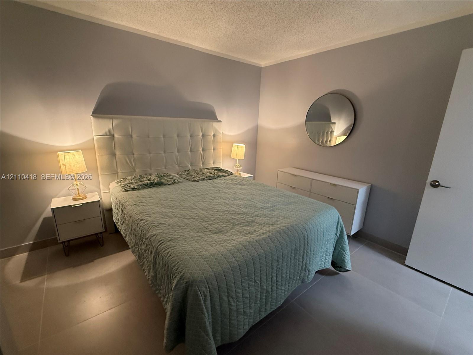 Neutral-toned wall finish, large-format tile flooring, and a circular wall-mounted mirror