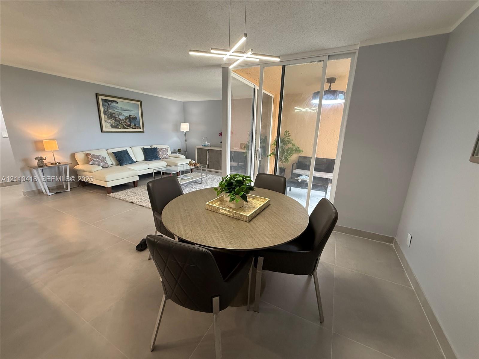Large-format tile flooring, modern geometric chandelier, and sliding glass door access to an enclosed patio