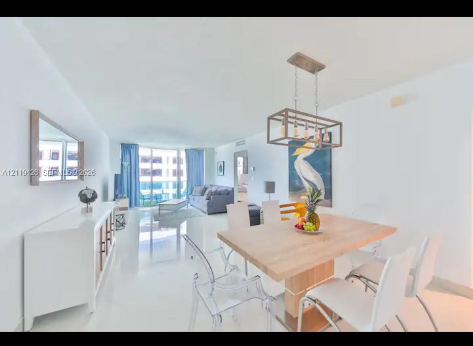 Open-concept living space featuring high-gloss tile flooring, floor-to-ceiling windows, and a structured metal-frame pendant light fixture Open-concept living space featuring high-gloss tile flooring, floor-to-ceiling windows, and a structured metal-frame pendant light fixture