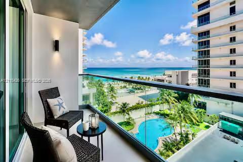 Covered balcony featuring a glass railing, wall-mounted exterior lighting, and overlooking a swimming pool and coastal waters