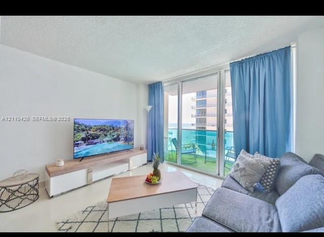Floor-to-ceiling glass sliding doors opening to a balcony with metal and glass railing, smooth finished ceilings, and neutral tile flooring