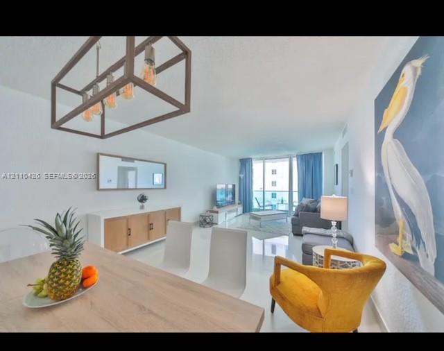 Open-concept main living area featuring glossy tile flooring, a geometric metal-frame chandelier, and floor-to-ceiling glass sliding doors Open-concept main living area featuring glossy tile flooring, a geometric metal-frame chandelier, and floor-to-ceiling glass sliding doors