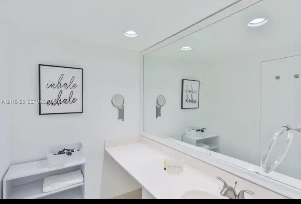 Large vanity with white countertop, recessed lighting, expansive wall-mounted mirror, and wall-mounted articulating vanity mirror