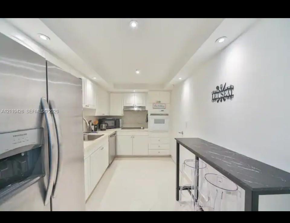 Kitchen featuring white shaker cabinetry, stainless steel refrigerator, recessed lighting, and a dark surface breakfast bar
