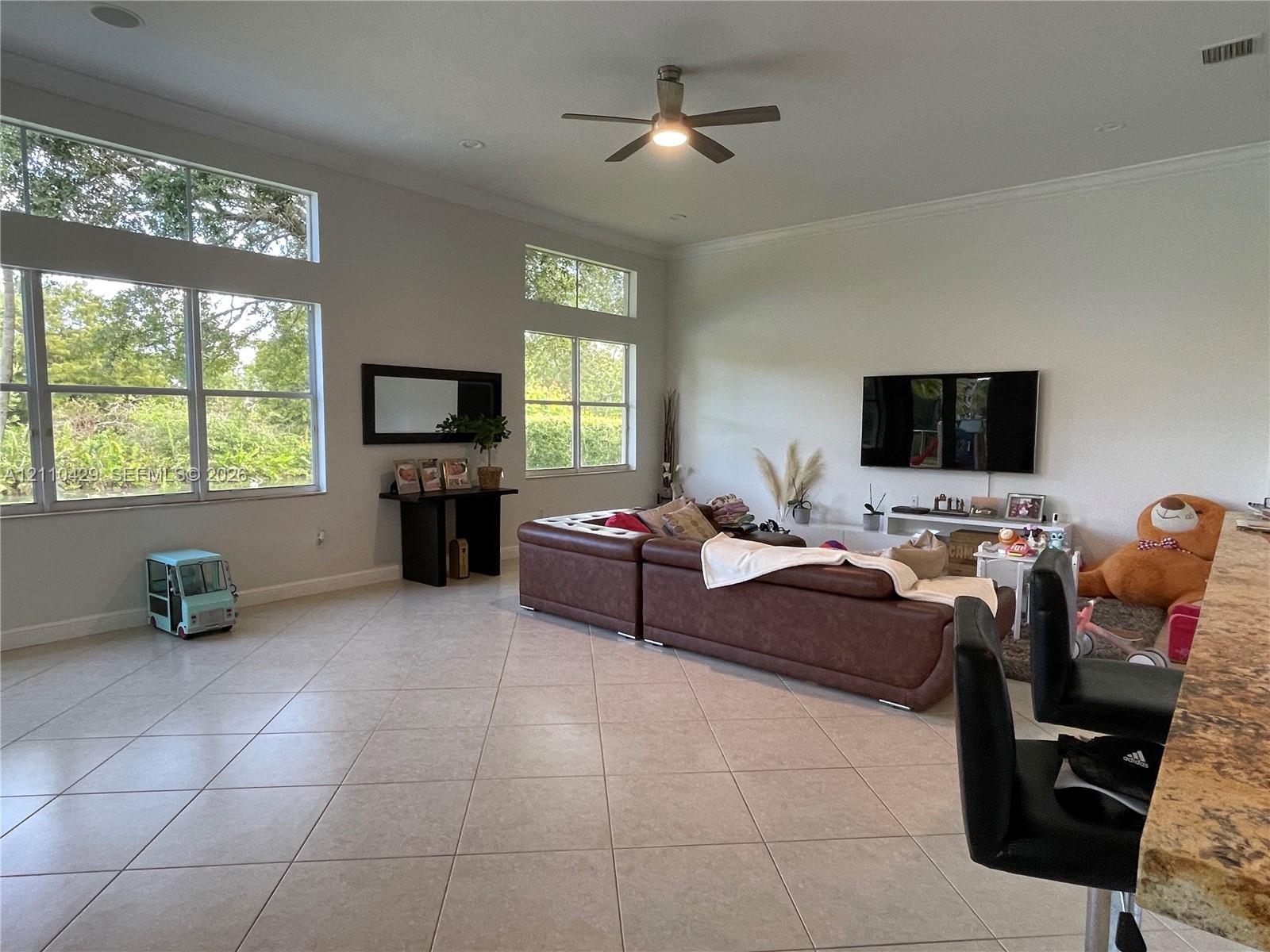 Spacious room featuring high ceilings, large windows with clerestory panes, tile flooring, and a ceiling fan