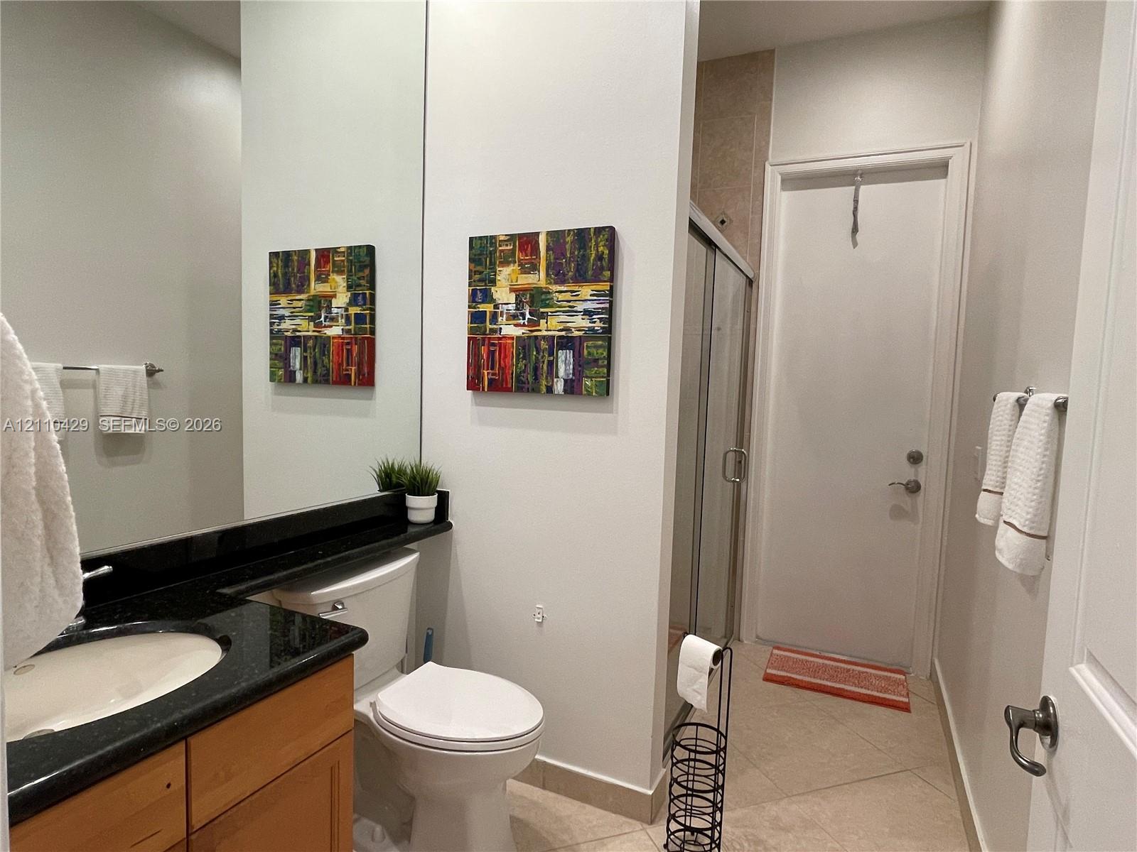 Bathroom featuring a vanity with dark stone countertop, integrated sink, wood-finish cabinetry, floor-to-ceiling mirror, and a glass-enclosed shower stall