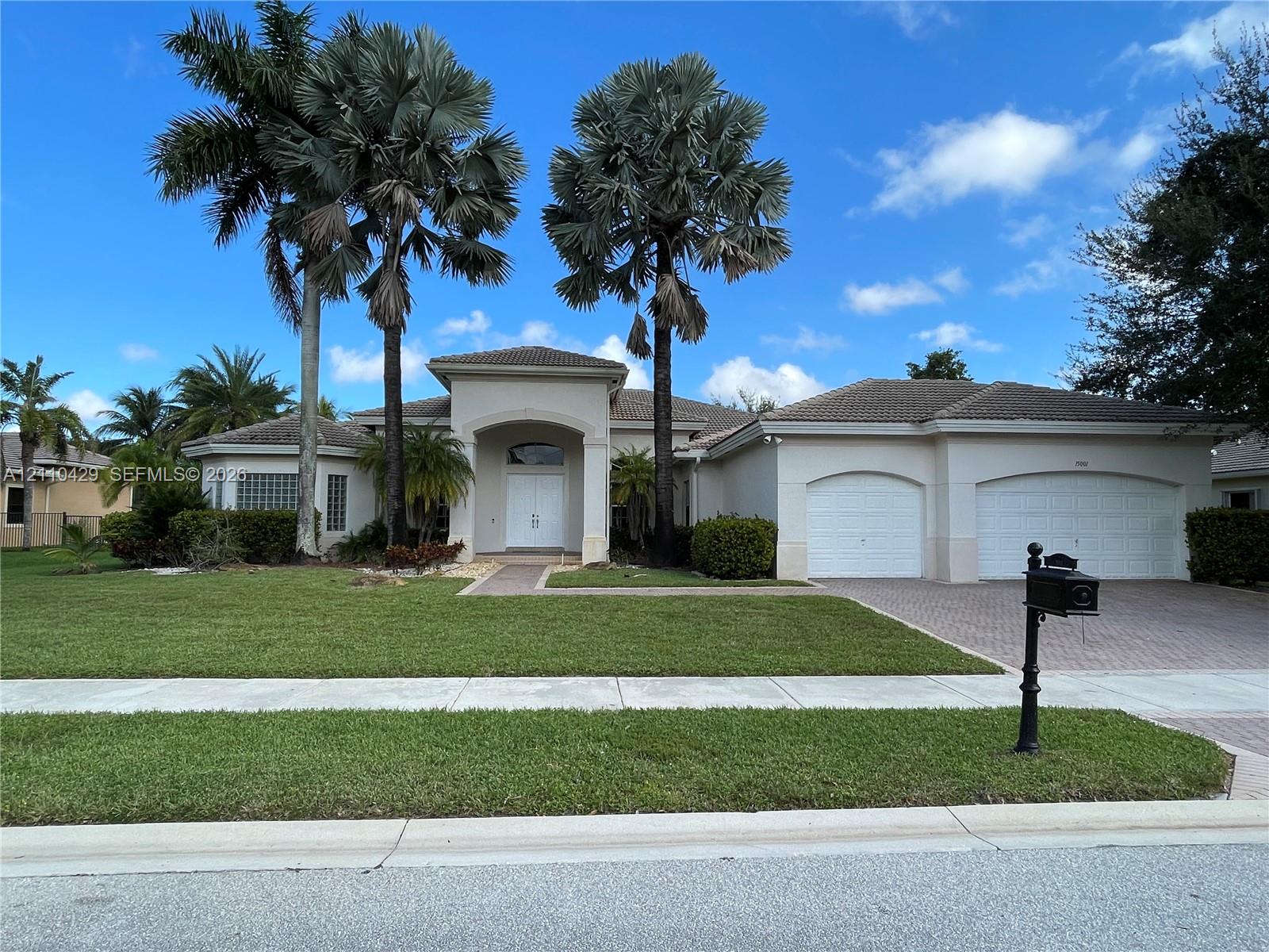 Stucco exterior residence featuring a covered entryway with arched roofline, dual-garage configuration, paver driveway, and mature palm trees