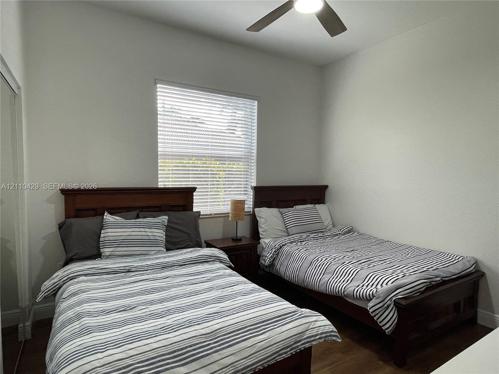 High-ceiling bedroom featuring wood-finish flooring, a central ceiling fan with integrated lighting, and horizontal window blinds