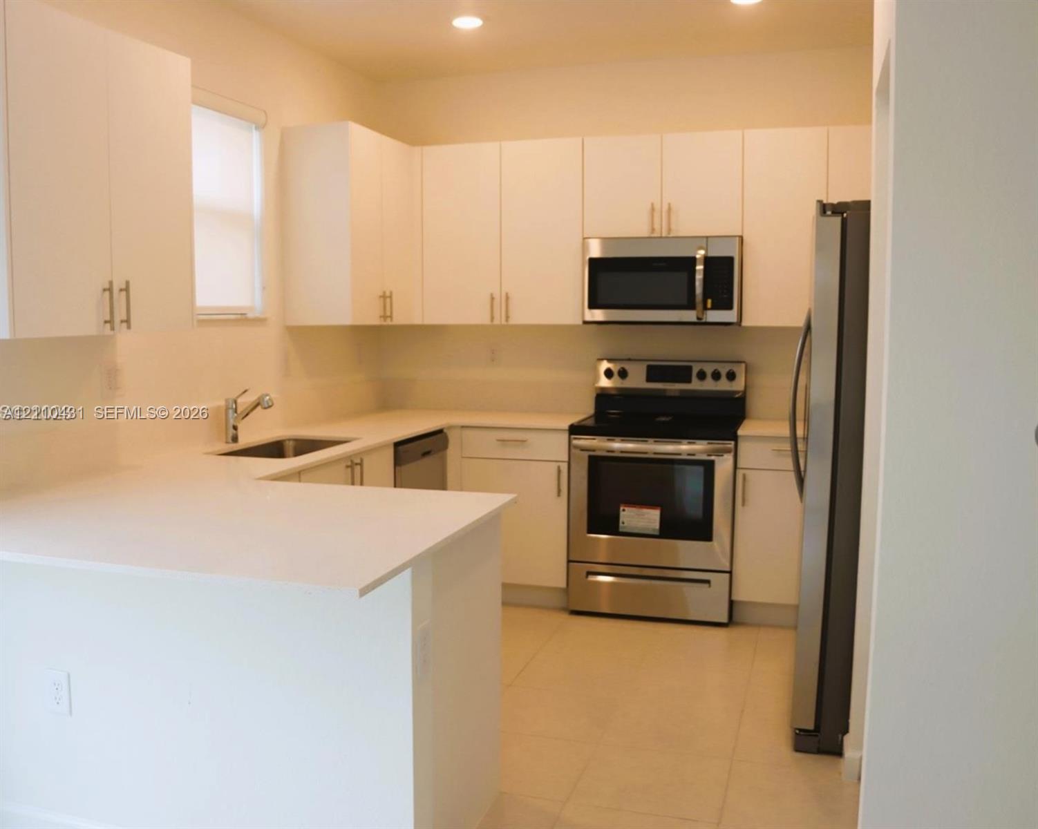 Kitchen featuring white flat-panel cabinetry, light-toned stone countertops, stainless steel appliances, and tile flooring