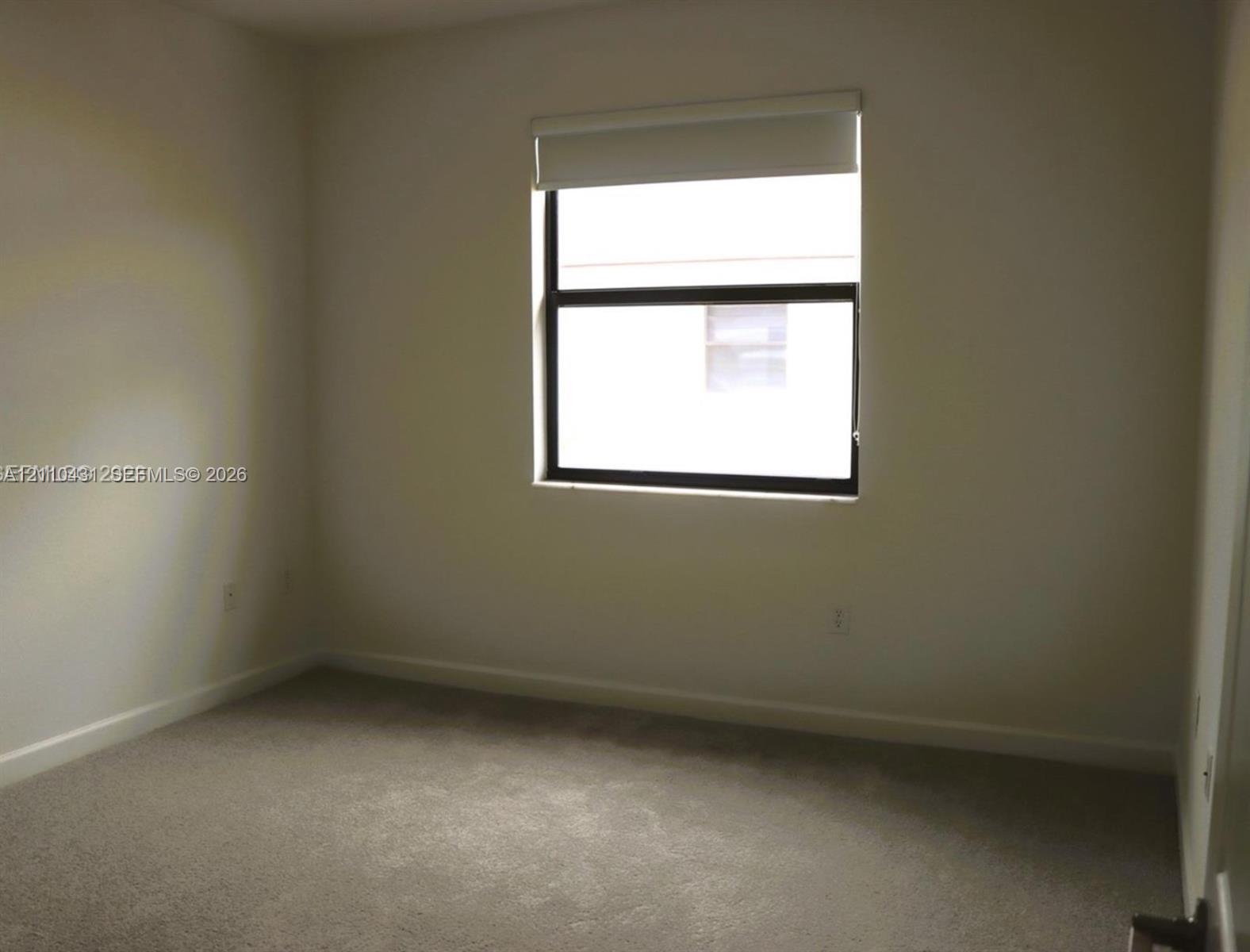 Neutral wall palette, wall-to-wall carpeting, single-pane window with dark framing, and fitted window shade