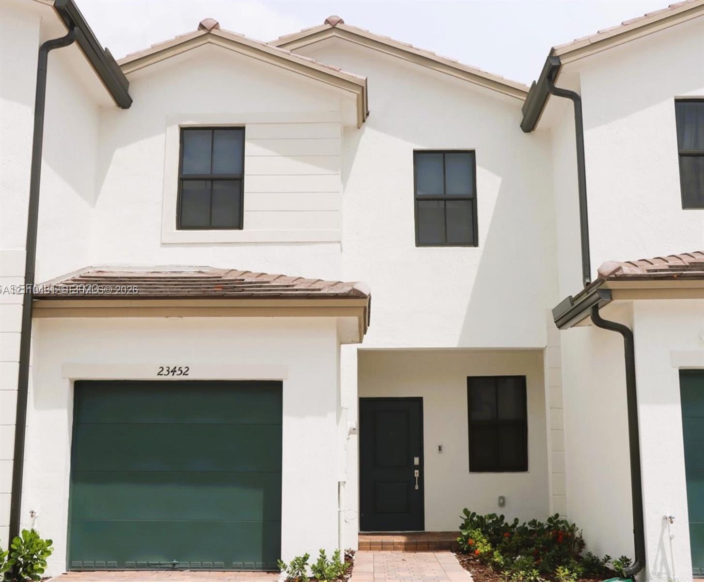 Exterior featuring a stucco facade, dark-toned garage door, gabled roofline, dark-framed multi-pane windows, and a paved entryway path Exterior featuring a stucco facade, dark-toned garage door, gabled roofline, dark-framed multi-pane windows, and a paved entryway path