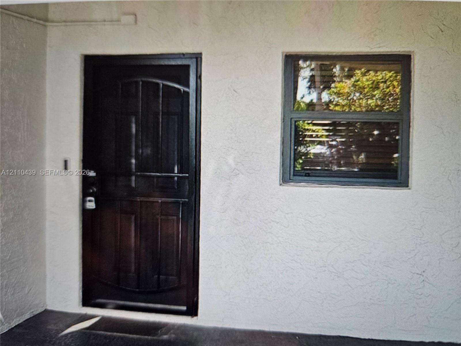 Entryway featuring a dark-finish security storm door, textured stucco exterior wall, and a single-hung window with dark-toned framing Entryway featuring a dark-finish security storm door, textured stucco exterior wall, and a single-hung window with dark-toned framing