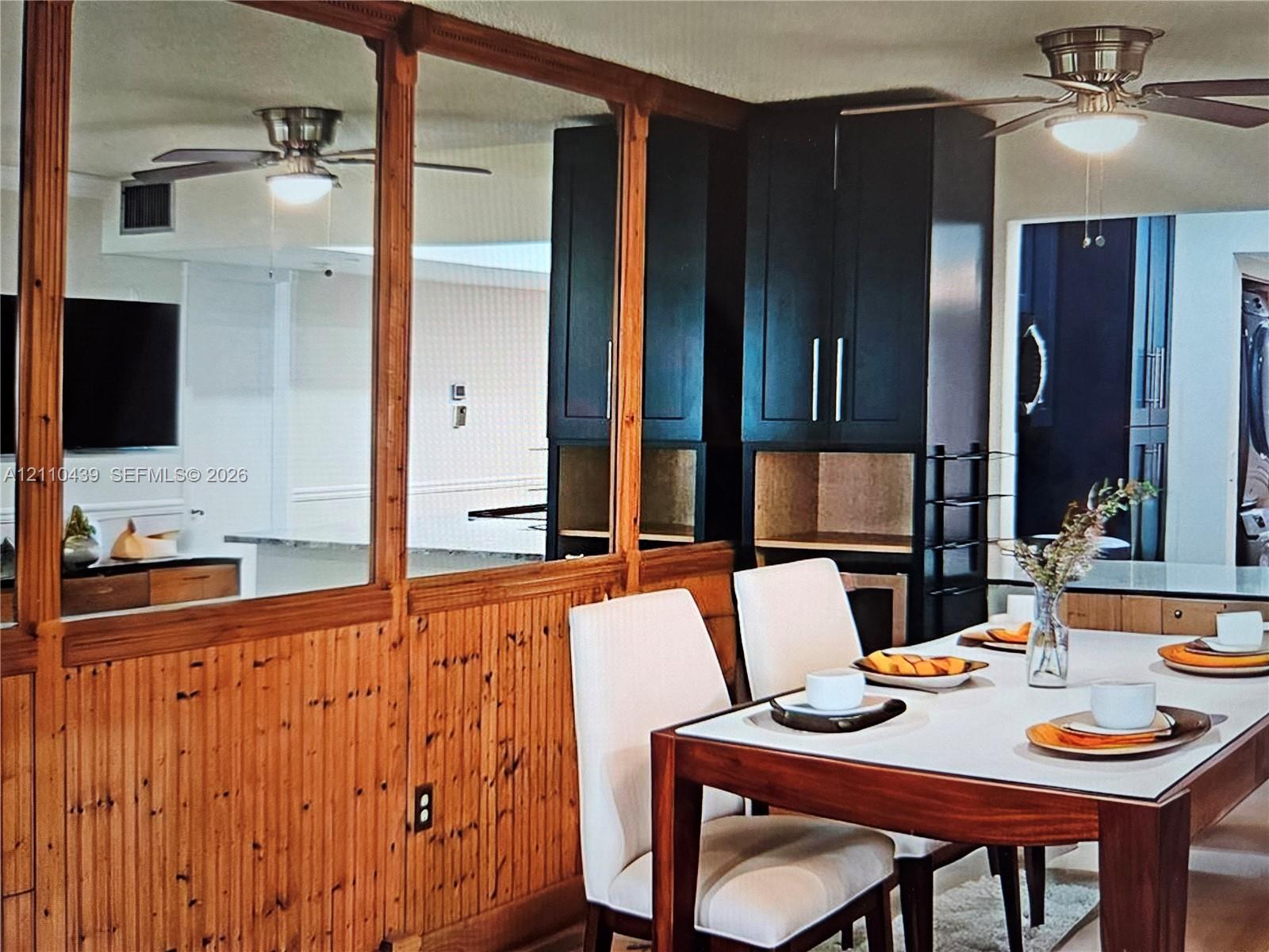 Mirror paneling with wood trim, beadboard wainscoting, matte bl built-in cabinetry, and ceiling-mounted light fixtures with integrated fans. Virtual Staging