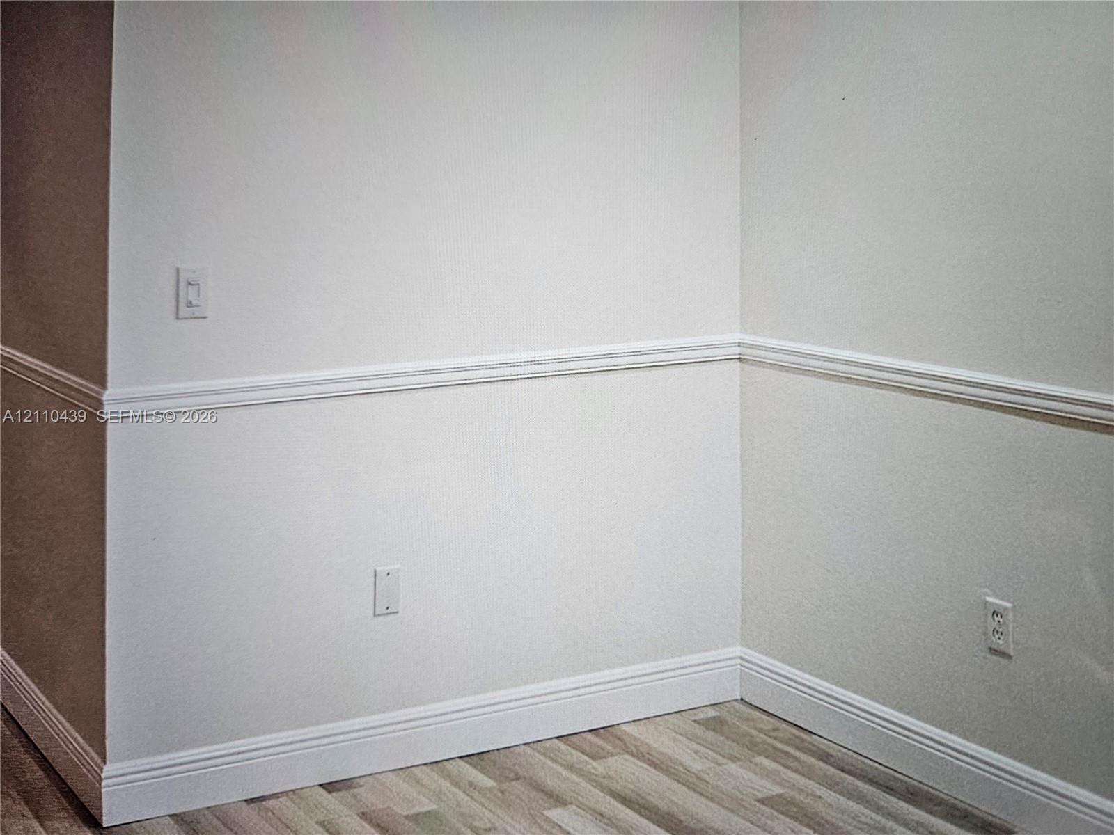 Interior corner featuring neutral wall paint, white chair rail molding, and wood-finish flooring