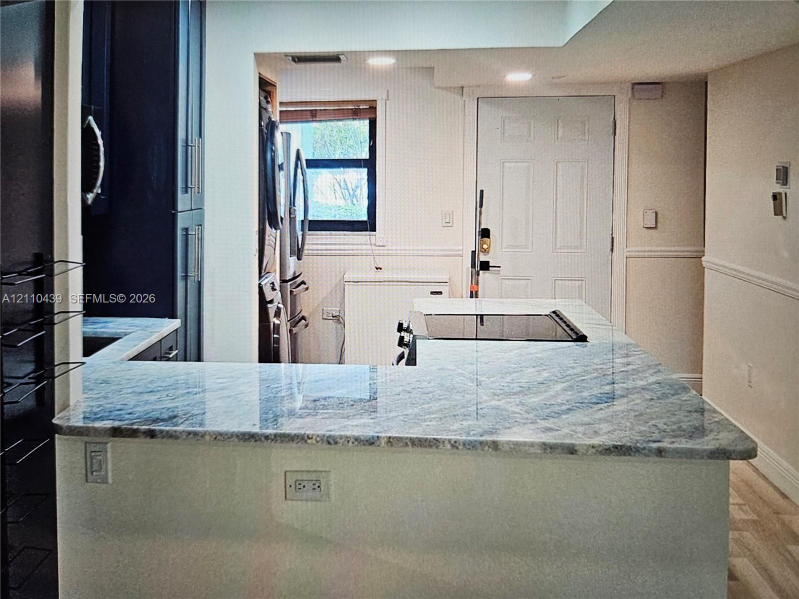 Kitchen featuring a stone-surface peninsula, dark cabinetry, a built-in cooktop, recessed lighting, and wood-finish flooring Kitchen featuring a stone-surface peninsula, dark cabinetry, a built-in cooktop, recessed lighting, and wood-finish flooring