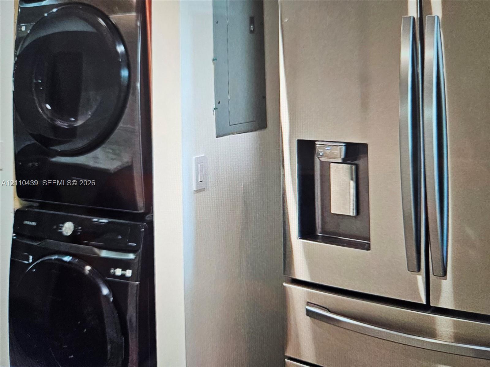 Stacked washer and dryer unit, stainless steel French door refrigerator with integrated water and ice dispenser, and wall-mounted electrical panel Stacked washer and dryer unit, stainless steel French door refrigerator with integrated water and ice dispenser, and wall-mounted electrical panel