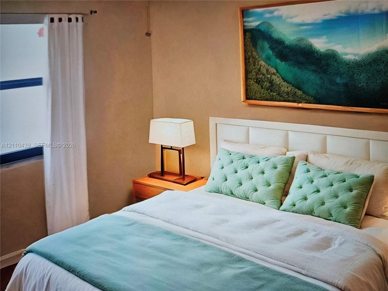 Bedroom featuring a paneled headboard and a window with horizontal trim. Virtual Staging