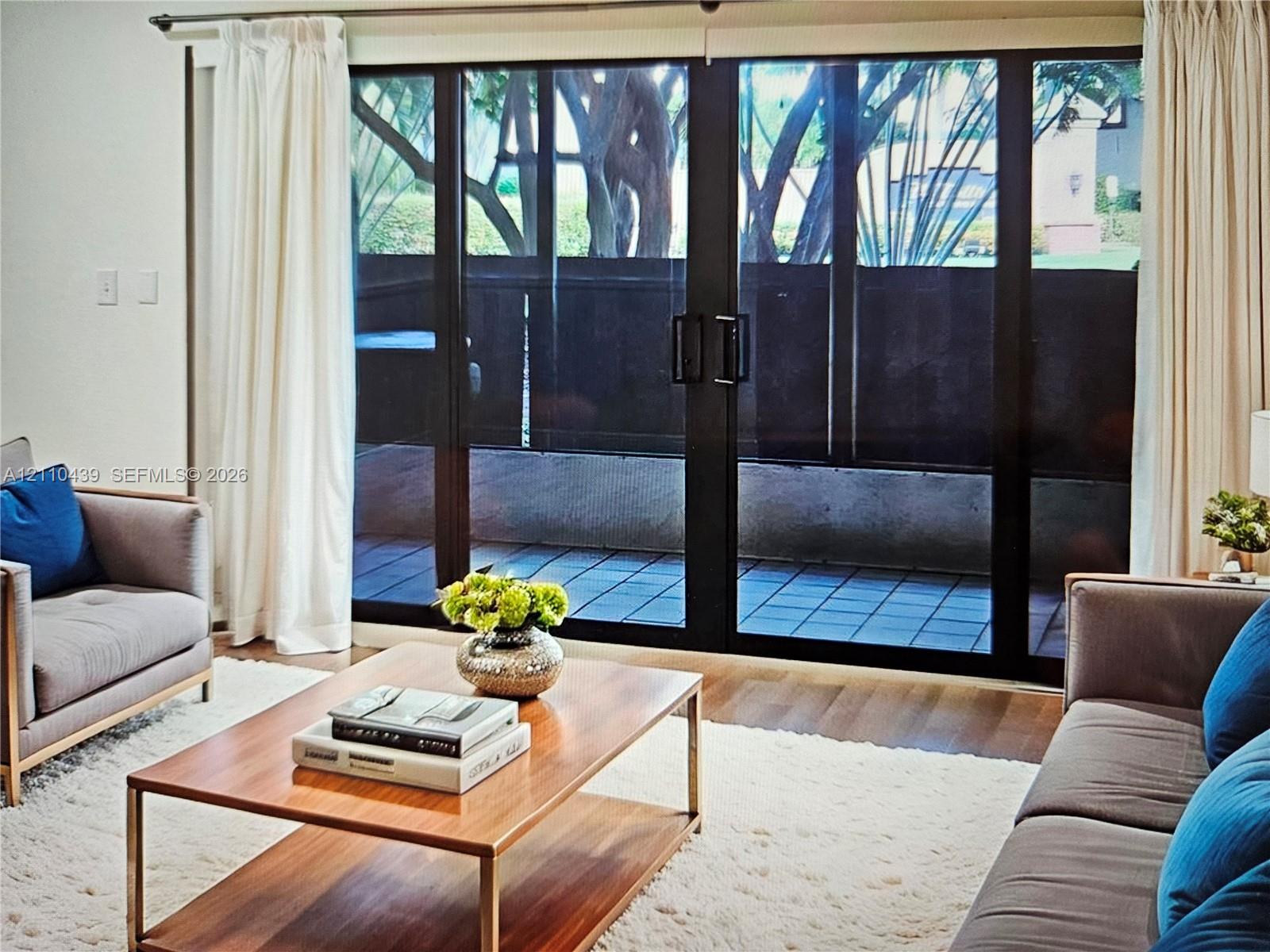 Floor-to-ceiling multi-panel sliding glass doors with black frames, wood-finish flooring, and a private paved patio. Virtual staging
