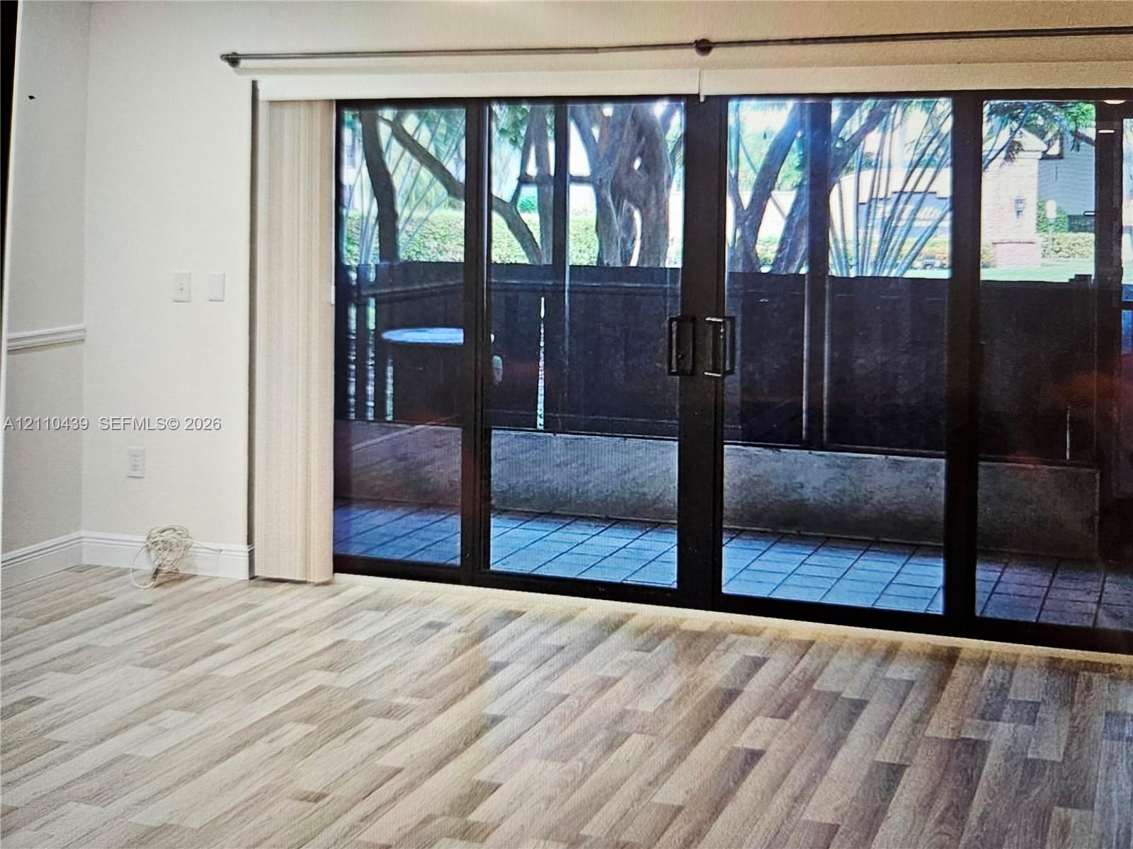 Wide-plank wood-finish flooring and floor-to-ceiling multi-panel sliding glass doors with dark metal frames opening to a private tiled patio