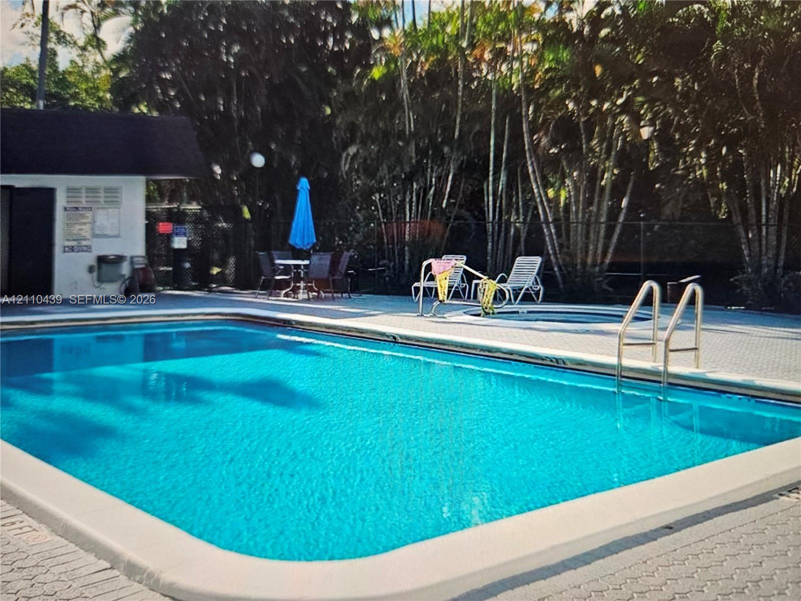 Swimming pool with surrounding paver deck, integrated spa, and mature palm trees