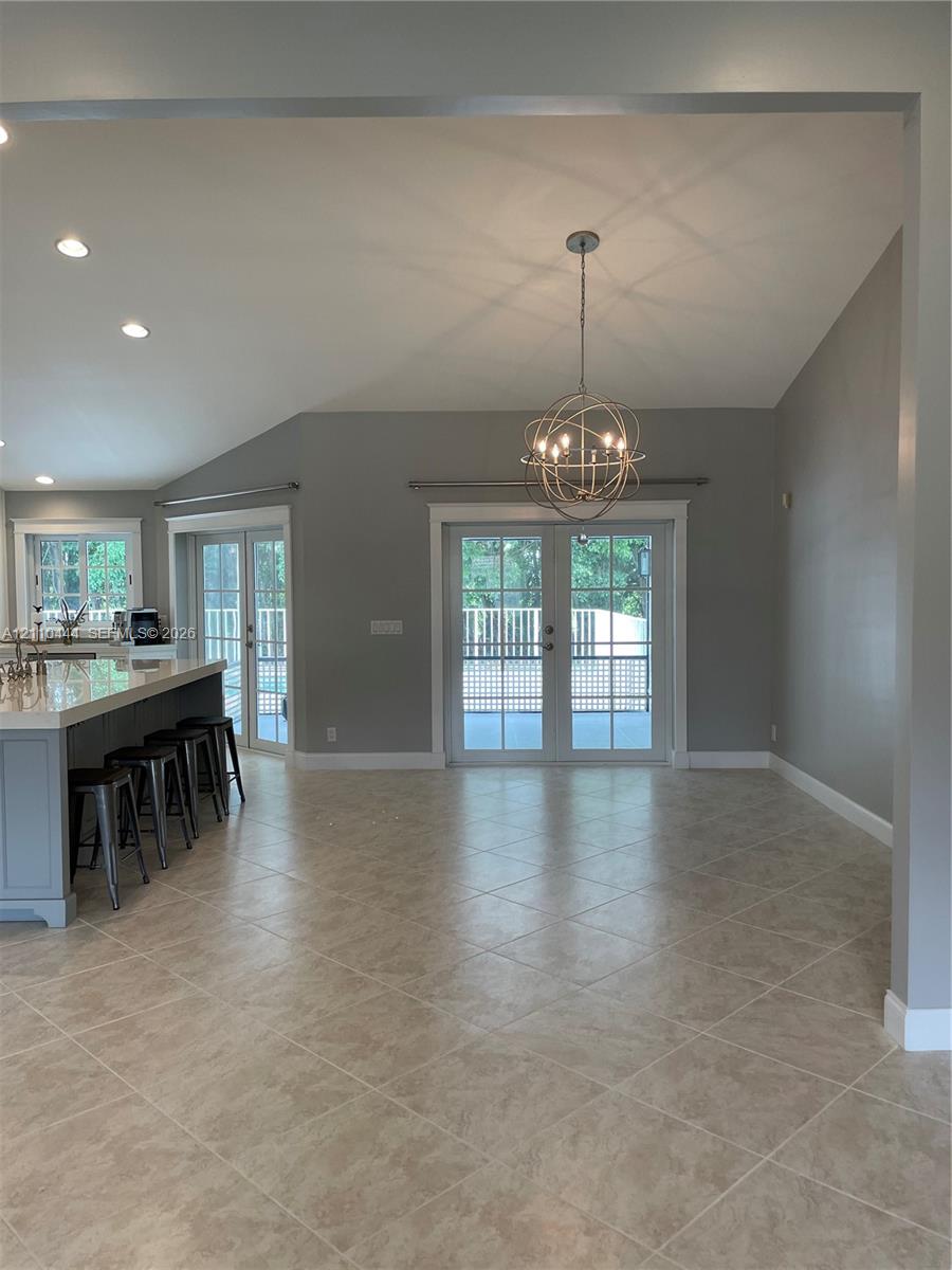 Open-concept interior featuring vaulted ceilings, tile flooring set on a diagonal, a kitchen island with a stone-finish countertop, a spherical metal chandelier, and French doors Open-concept interior featuring vaulted ceilings, tile flooring set on a diagonal, a kitchen island with a stone-finish countertop, a spherical metal chandelier, and French doors