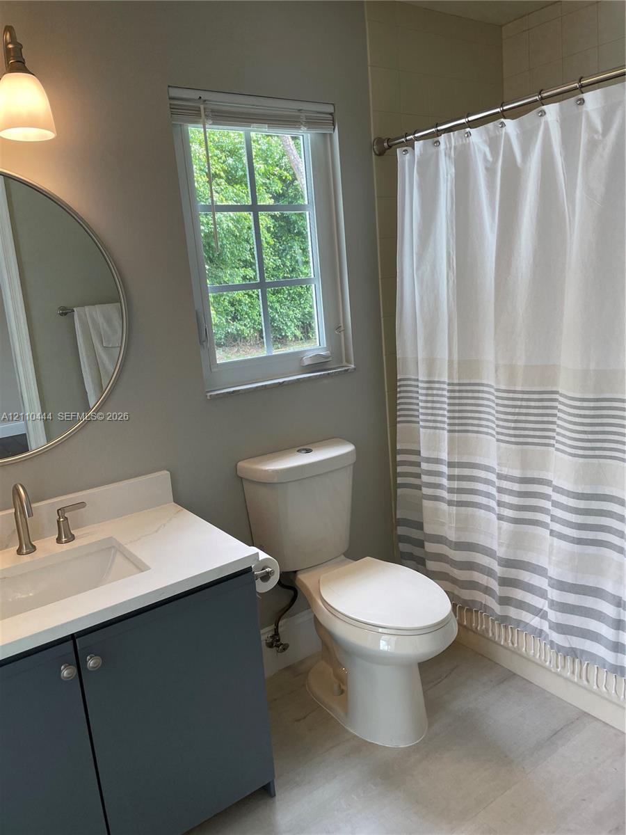 Bathroom featuring a charcoal-toned vanity with a white countertop, circular wall-mounted mirror, single-handle brushed nickel faucet, and wood-finish flooring
