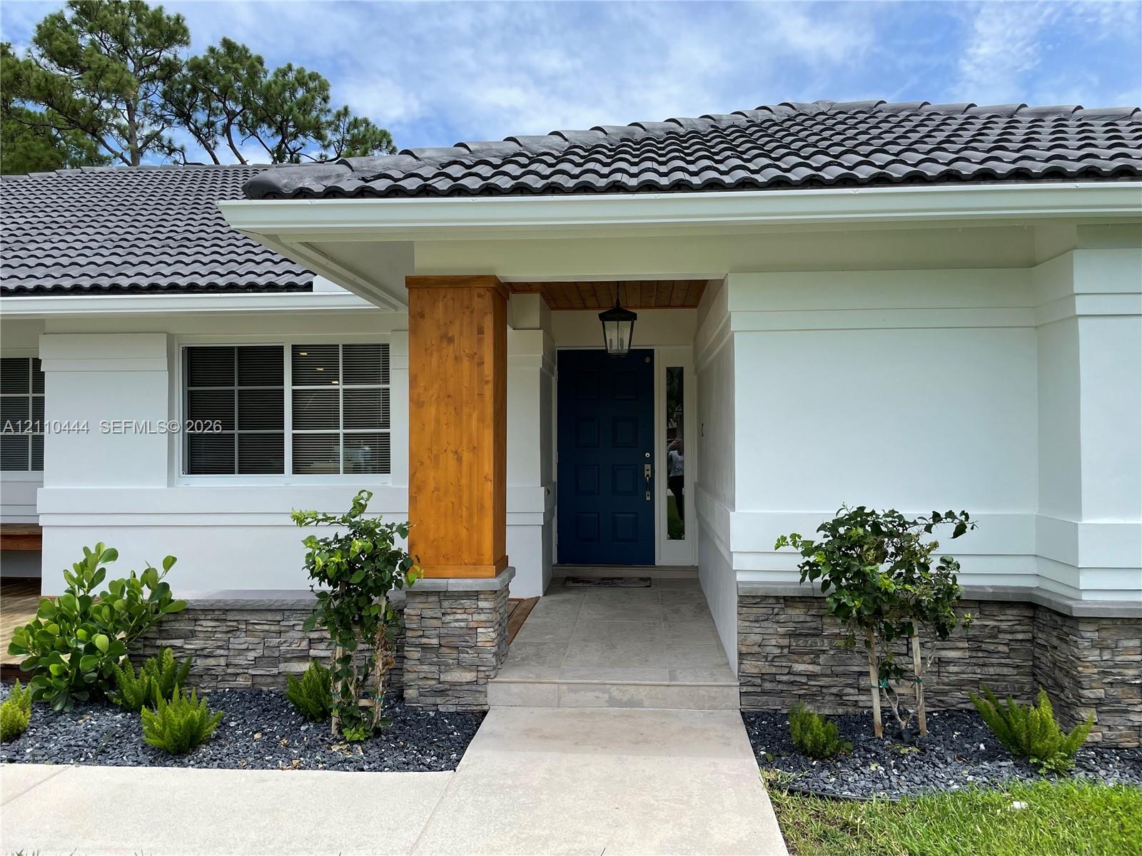 Exterior featuring a dark tile roof, smooth-finish white facade, stone veneer accents, prominent wood-finish support pillar, and a solid-panel front door