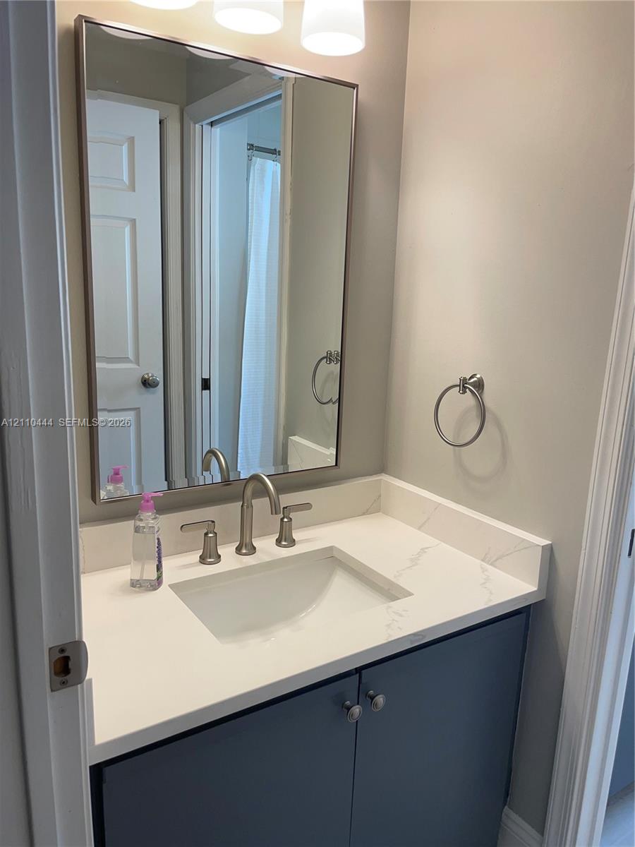 Bathroom vanity featuring a stone-composite countertop with integrated sink, polished chrome widespread faucet, navy blue cabinetry, and a framed rectangular wall mirror