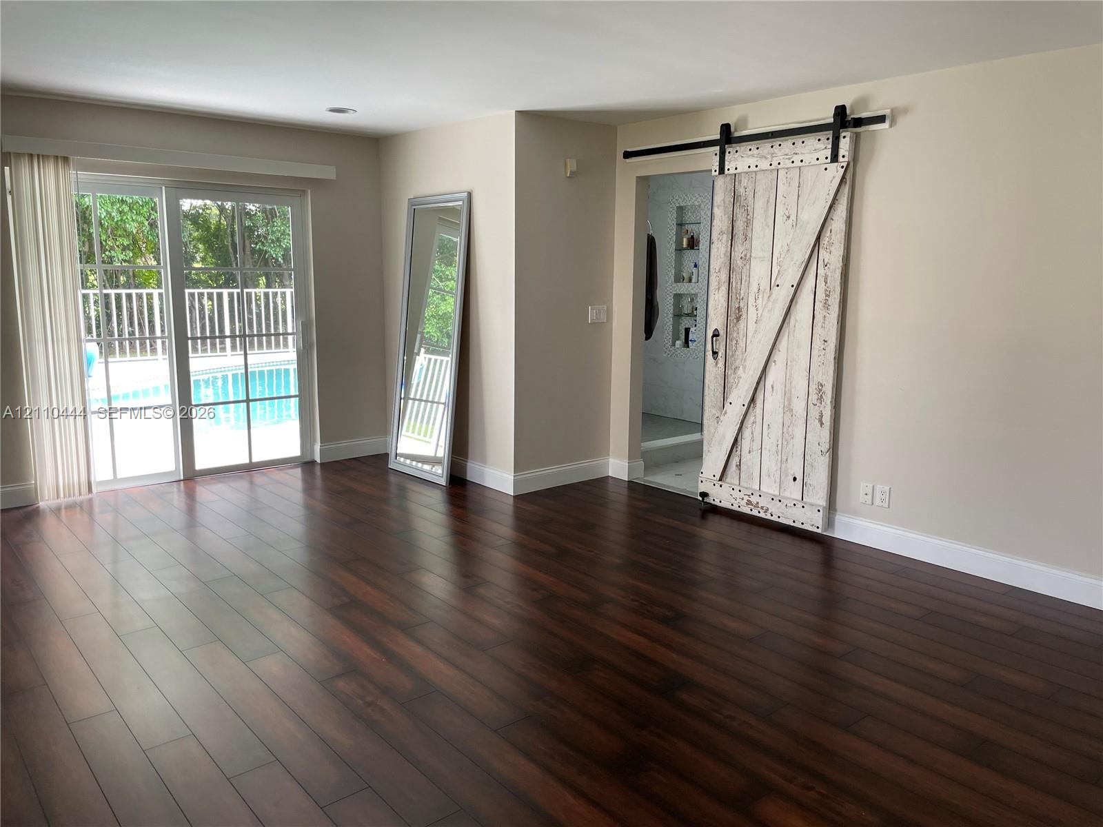 Dark wood-finish flooring, sliding glass door with exterior pool access, and distressed white-finish barn door with matte black hardware Dark wood-finish flooring, sliding glass door with exterior pool access, and distressed white-finish barn door with matte black hardware