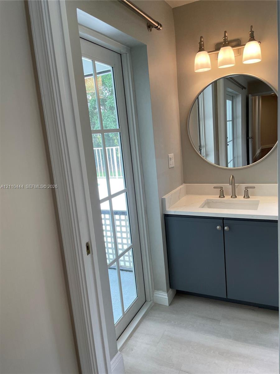 Vanity featuring a solid-surface countertop, integrated rectangular sink, dark cabinetry with hardware, a circular wall-mounted mirror, and a three-light fixture