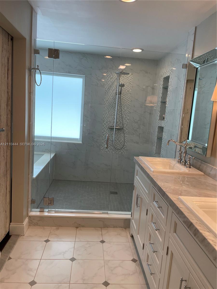Walk-in shower featuring glass paneling, floor-to-ceiling tile, and built-in shelving, paired with a dual-sink vanity with stone-finish countertops and polished metal fixtures