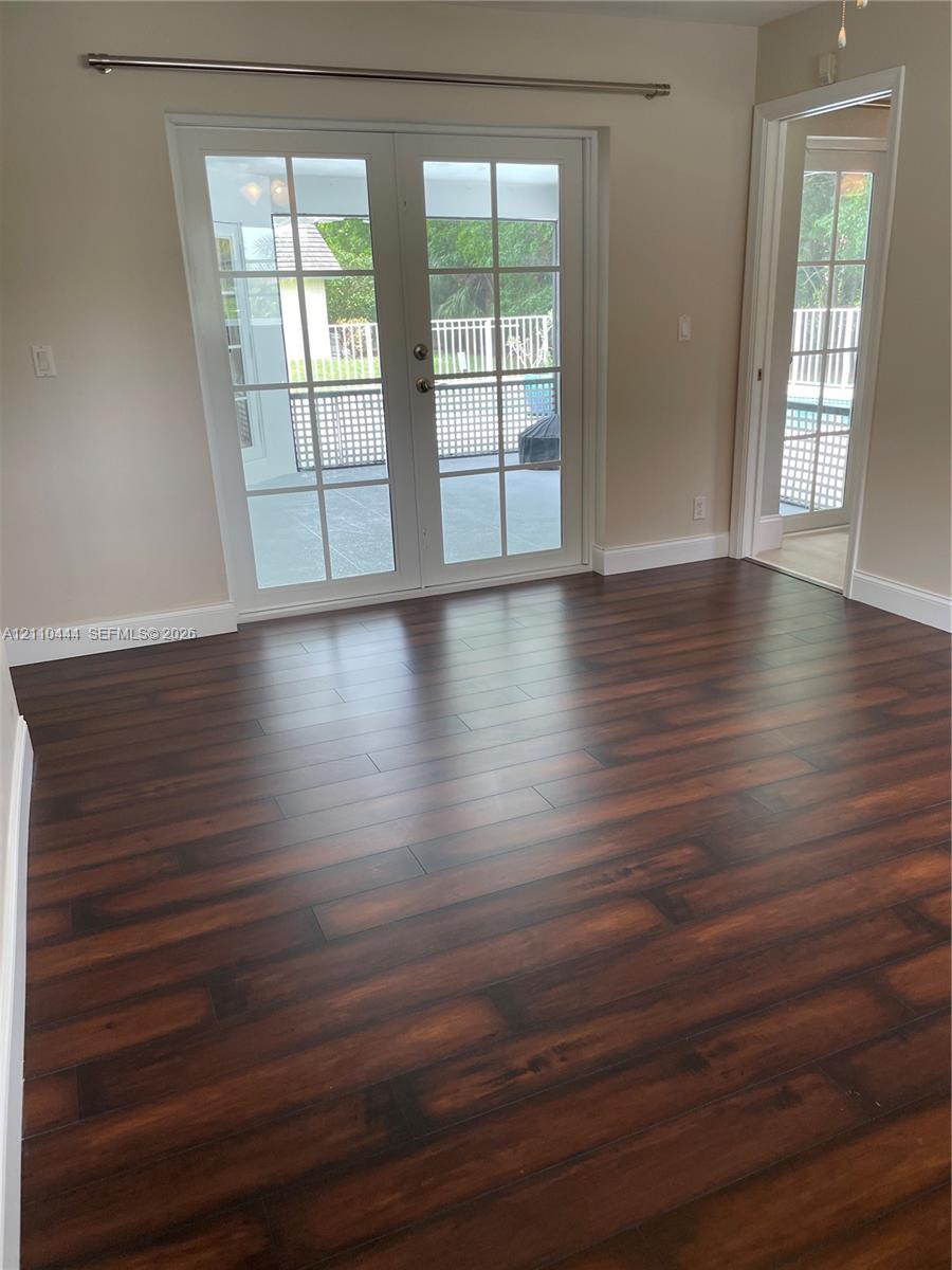 Room with dark wood-finish flooring, white-trimmed French doors with glass panes, and a separate doorway featuring a matching glass-paned door