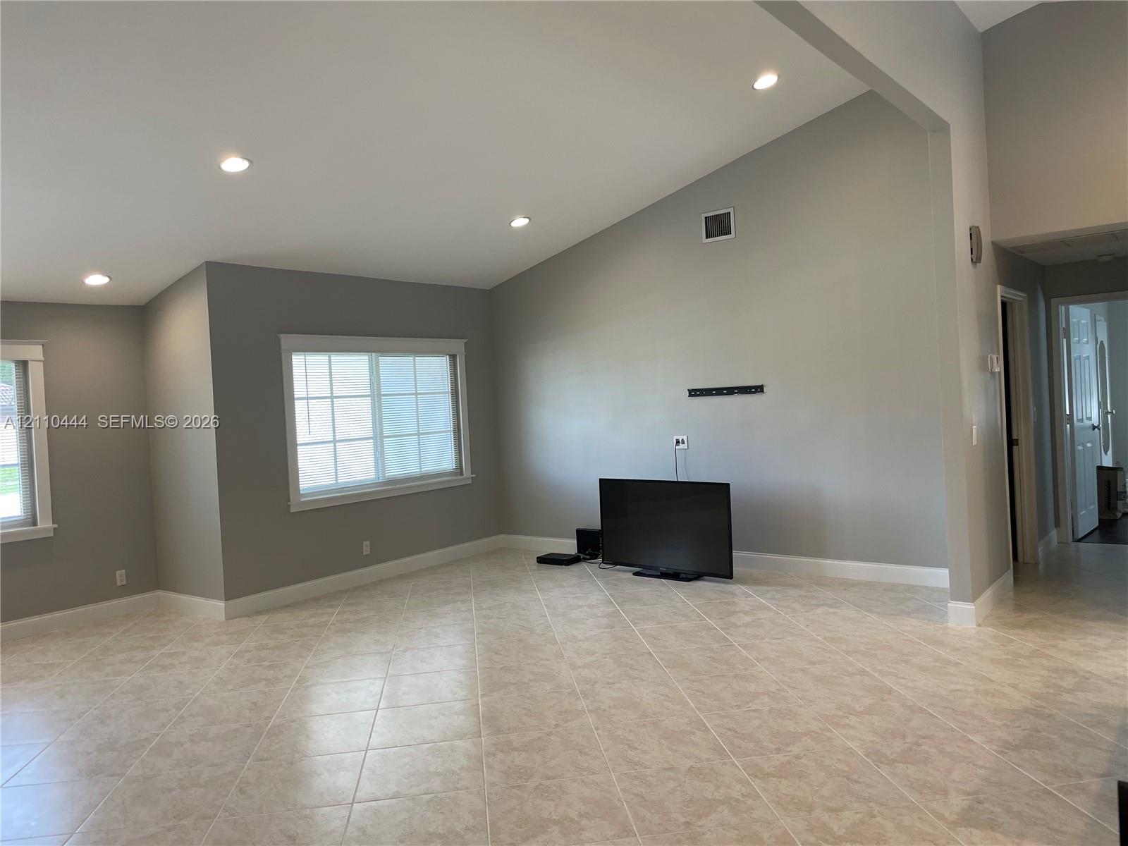 Vaulted ceilings featuring recessed lighting, large grid-style windows, and neutral-tone tile flooring Vaulted ceilings featuring recessed lighting, large grid-style windows, and neutral-tone tile flooring