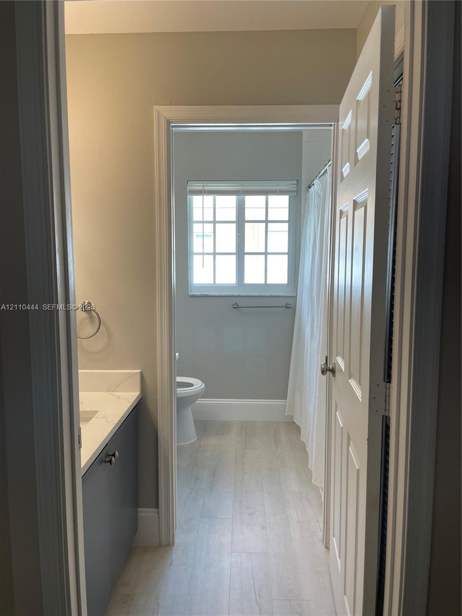 Bathroom featuring wood-finish flooring, a charcoal-toned vanity with a light-colored solid surface countertop, and a multi-pane window