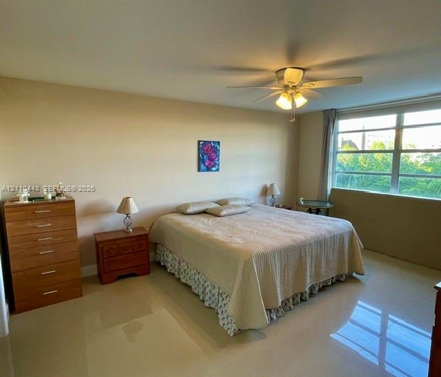 Spacious room featuring neutral wall tones, polished tile flooring, a multi-blade ceiling fan with integrated lighting, and expansive windows