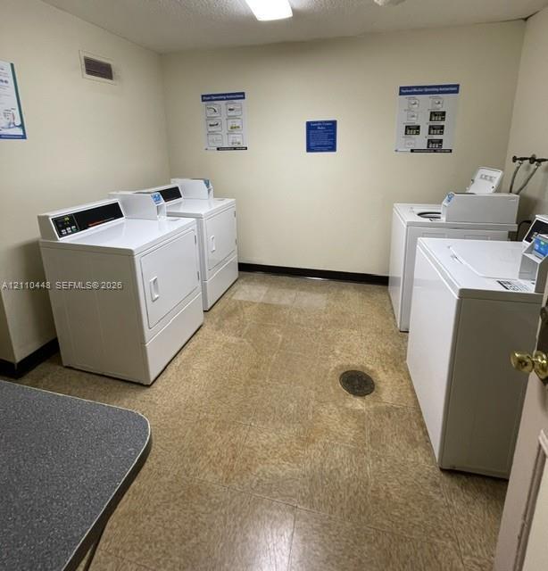 Laundry room featuring dual sets of white top-load washers and front-load dryers, resilient tile flooring, and overhead flush-mount lighting