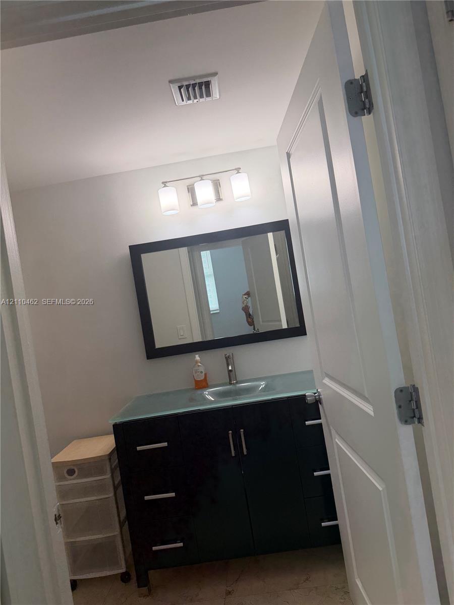Dark wood-finish vanity featuring a light-toned countertop with integrated sink, rectangular mirror with a dark frame, and a three-light vanity fixture