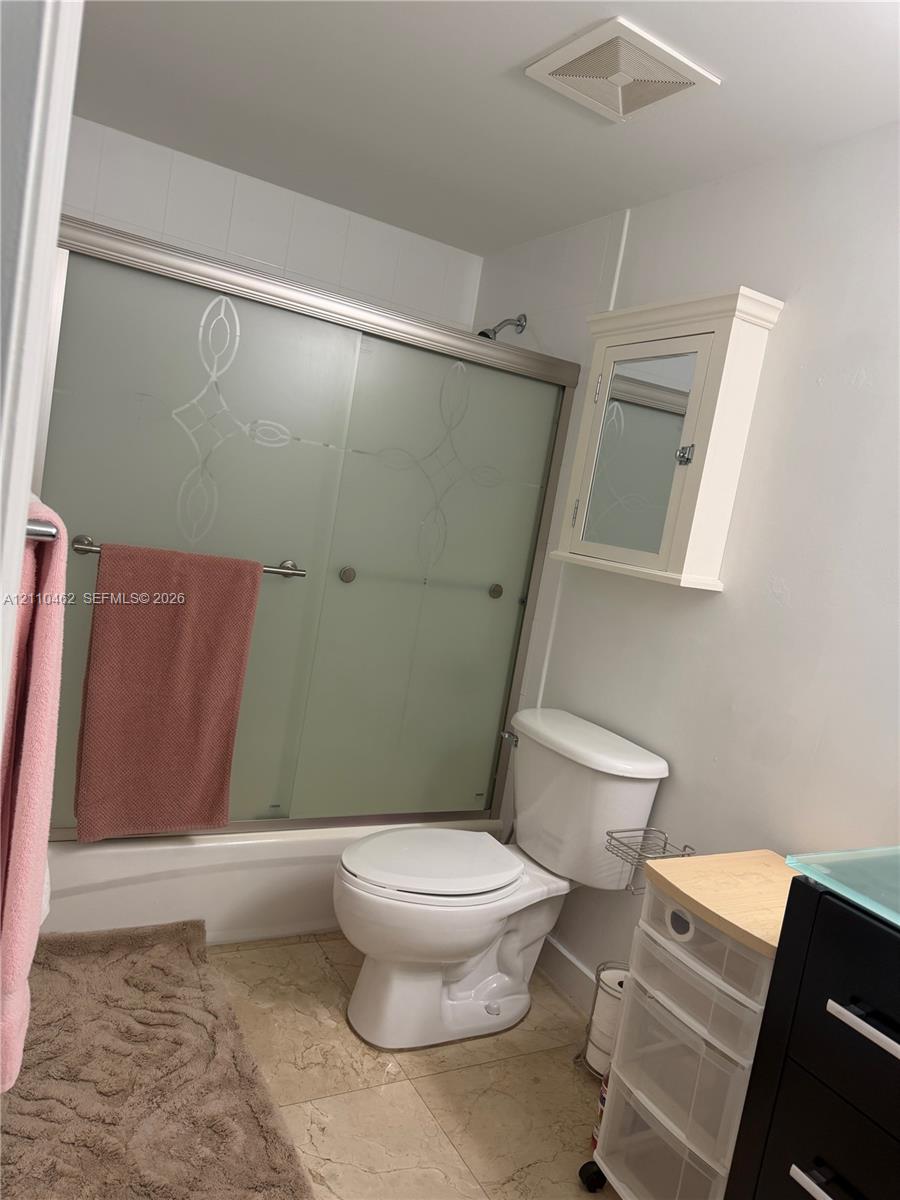 Bathtub with frosted glass sliding enclosure featuring decorative etching, wall-mounted medicine cabinet, and tile flooring