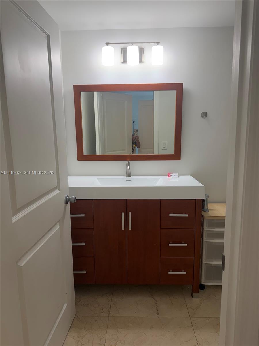 Vanity featuring wood-finish cabinetry, a rectangular white sink, a solid surface countertop, a matching wood-frame mirror, and a three-light fixture