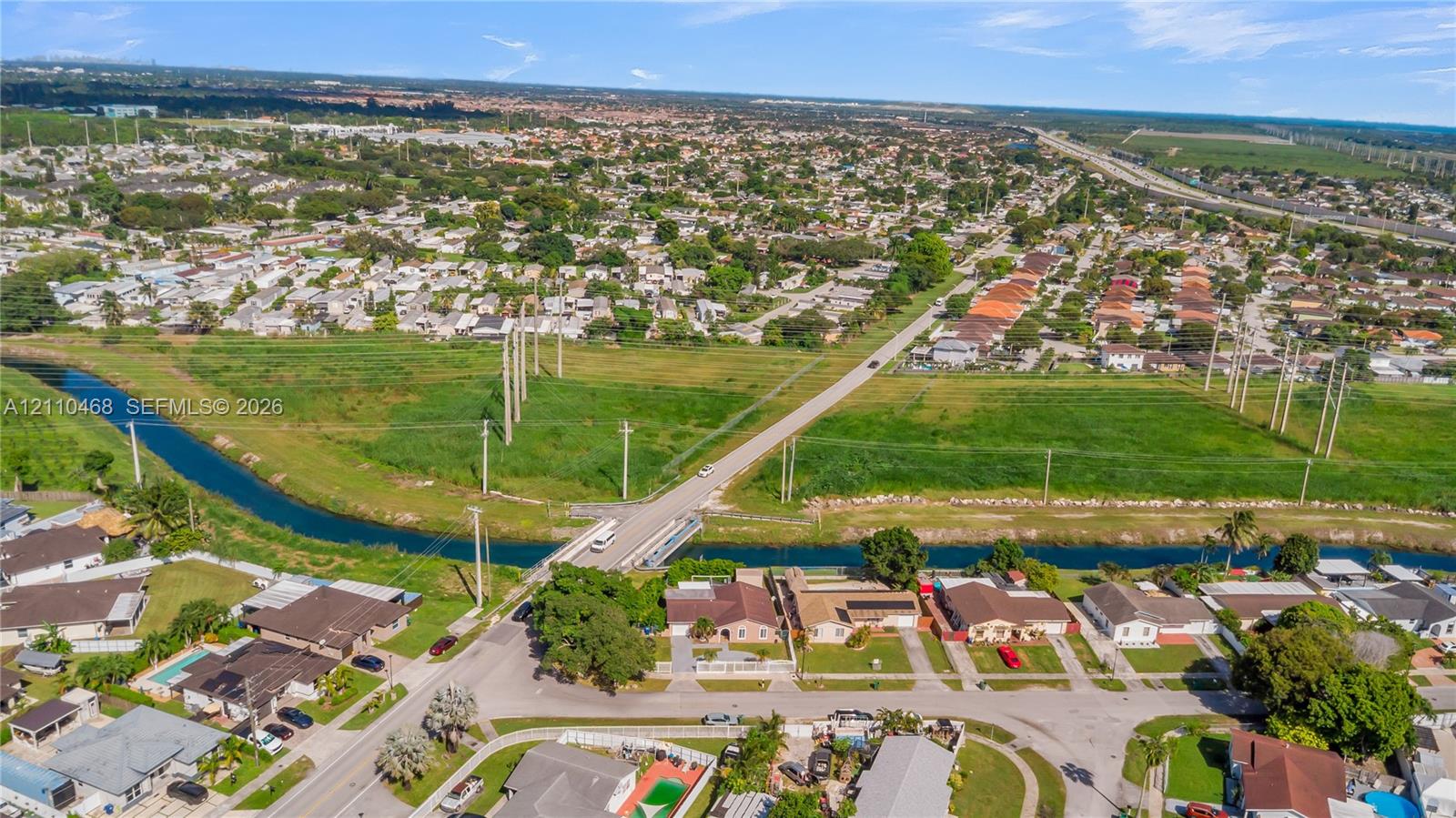 Aerial perspective of the residential area featuring a linear waterway, paved street access, mature trees, and established suburban development