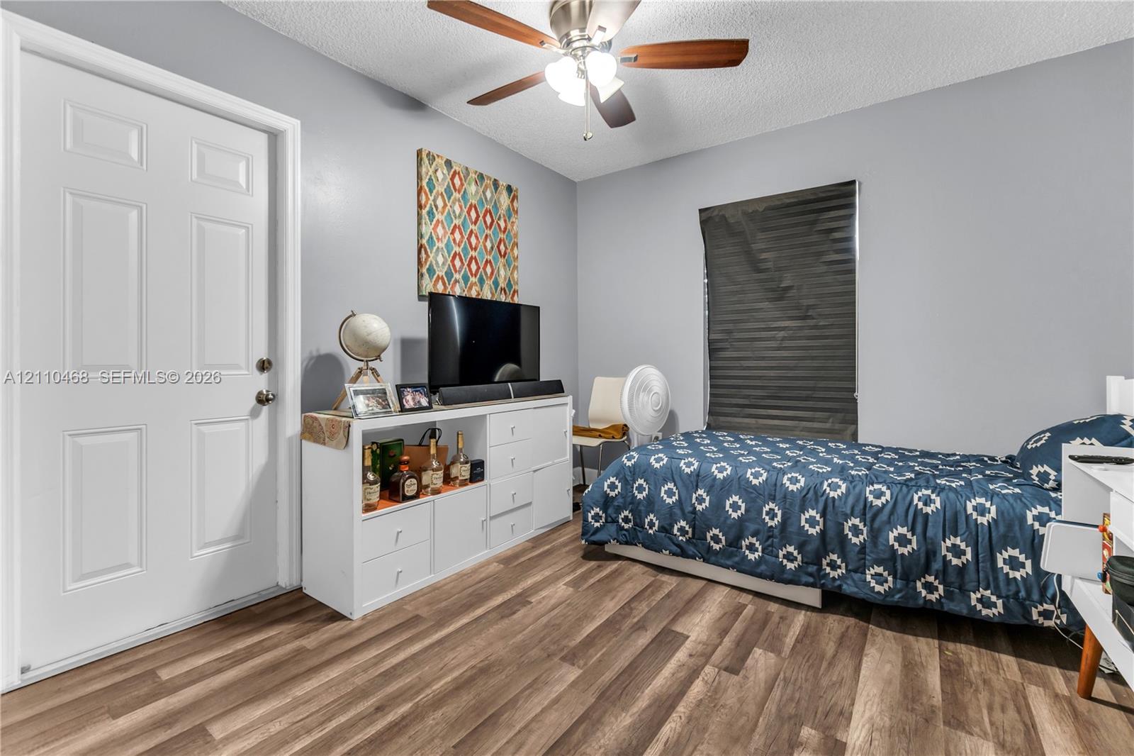 Room featuring wood-finish flooring, a six-panel door, and a ceiling fan with integrated lighting