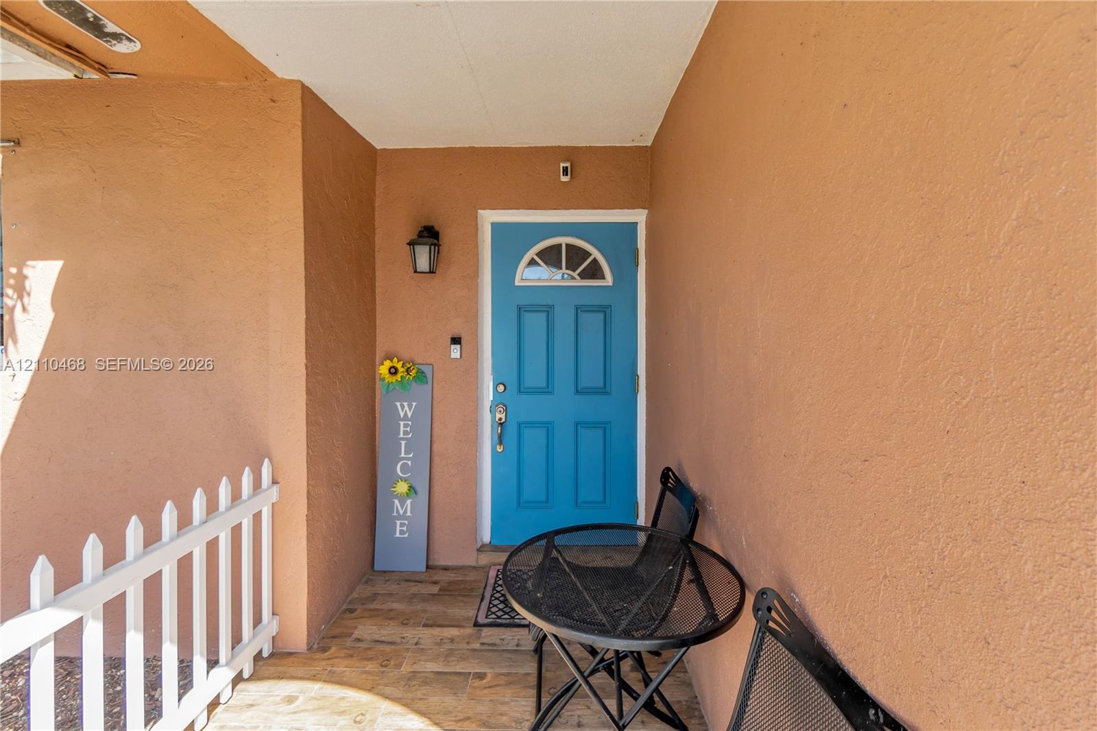 Covered entryway featuring a blue front door with a semicircular transom window, wall-mounted exterior lighting, and wood-finish flooring Covered entryway featuring a blue front door with a semicircular transom window, wall-mounted exterior lighting, and wood-finish flooring